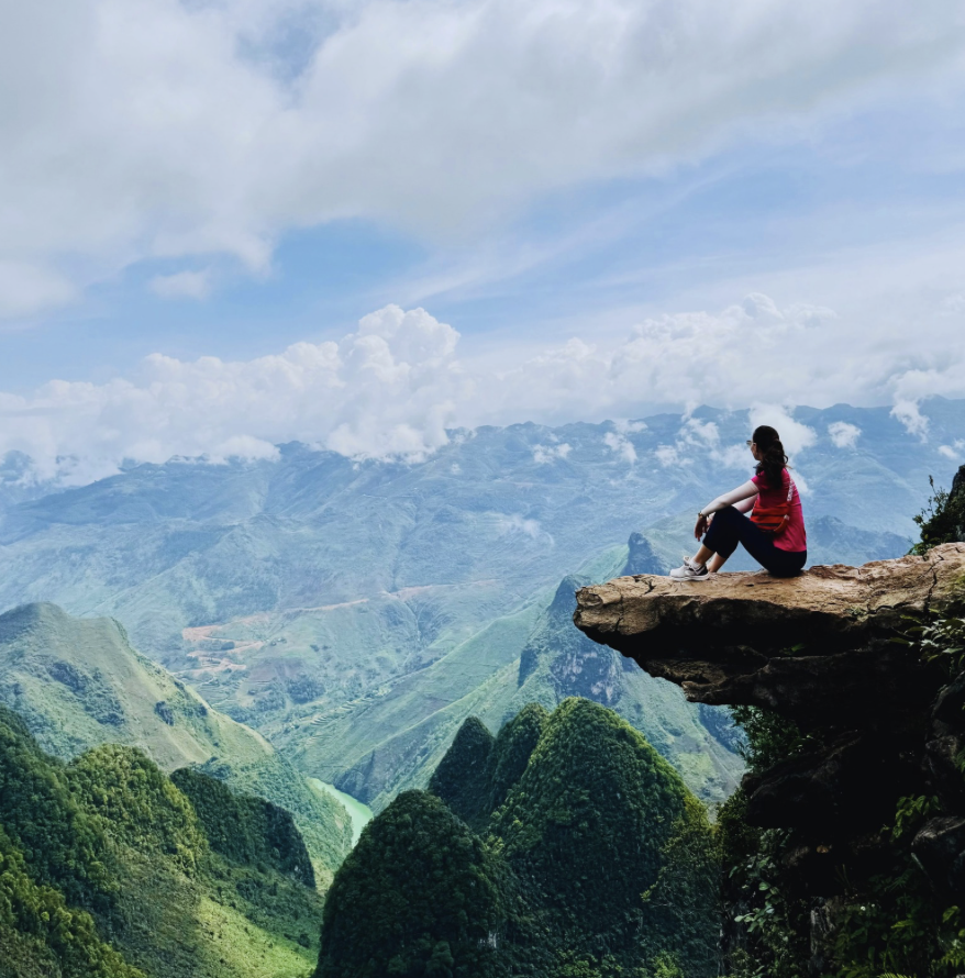 Woman sitting alone on a rocky cliff edge overlooking the vast green mountains of Ha Giang, northern Vietnam