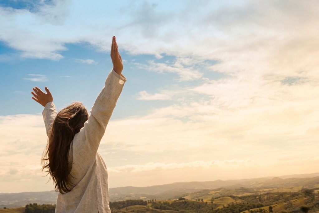 Woman with arms raised toward the sky outdoors, representing the sense of freedom and lightness after releasing subconscious patterns