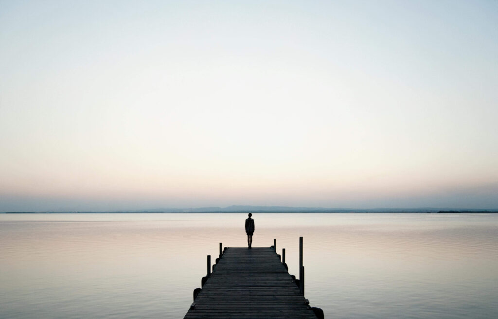 Person standing at the end of a pier overlooking calm water at dusk, representing the inner clarity and openness that follows energetic reprogramming work