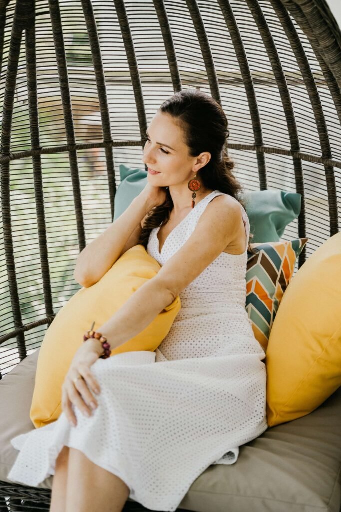 A woman sits relaxed and smiling within the curved, cage-like frame of a woven chair, a gentle image of how a limited identity can feel comfortable rather than confining